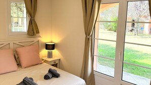 Ein Schlafzimmer mit Bett, Kissen, einer Lampe, einem Fenster und Blick ins Freie.