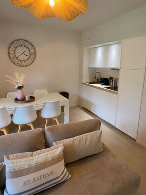 A modern kitchen with white cabinets, a dining area with a white table and chairs, and a sofa with a cushion labeled 'ST. RAPHAEL'. - Air-conditioned apartment with a heated pool, 10 minutes from Saint-Tropez (Grimaud)