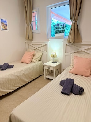 A hotel room with two beds, a nightstand with a lamp, and a window with curtains. - Air-conditioned apartment with a heated pool, 10 minutes from Saint-Tropez (Grimaud)