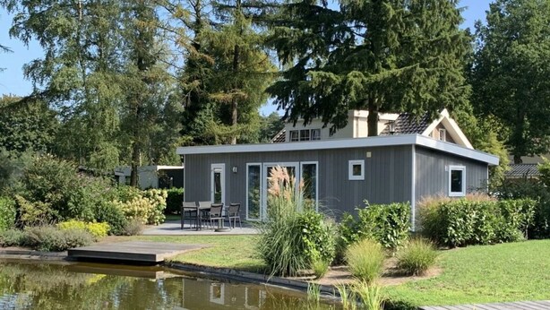 A modern house with a pond, deck, and outdoor seating area.