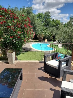 Un patio con mobiliario exterior, piscina y abundante vegetación.