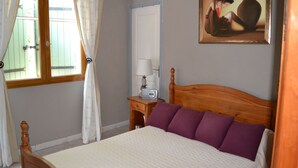 A bedroom with a wooden bed, a nightstand with a lamp, a painting on the wall, and a window with curtains. - House with swimming pool, terraces and exceptional views. (Lunas-les-Châteaux)