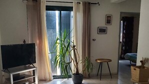 A living room with a TV, sofa, glass coffee table, potted plants, and a sliding glass door leading to a balcony. - House with swimming pool, terraces and exceptional views. (Lunas-les-Châteaux)