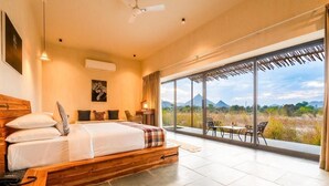 A bedroom with a large bed, a view of the outdoors, and a dining area with chairs.