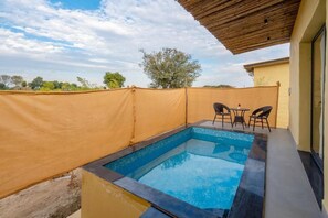 A swimming pool with a wooden pergola overhead, surrounded by a beige fence, and a table with chairs.