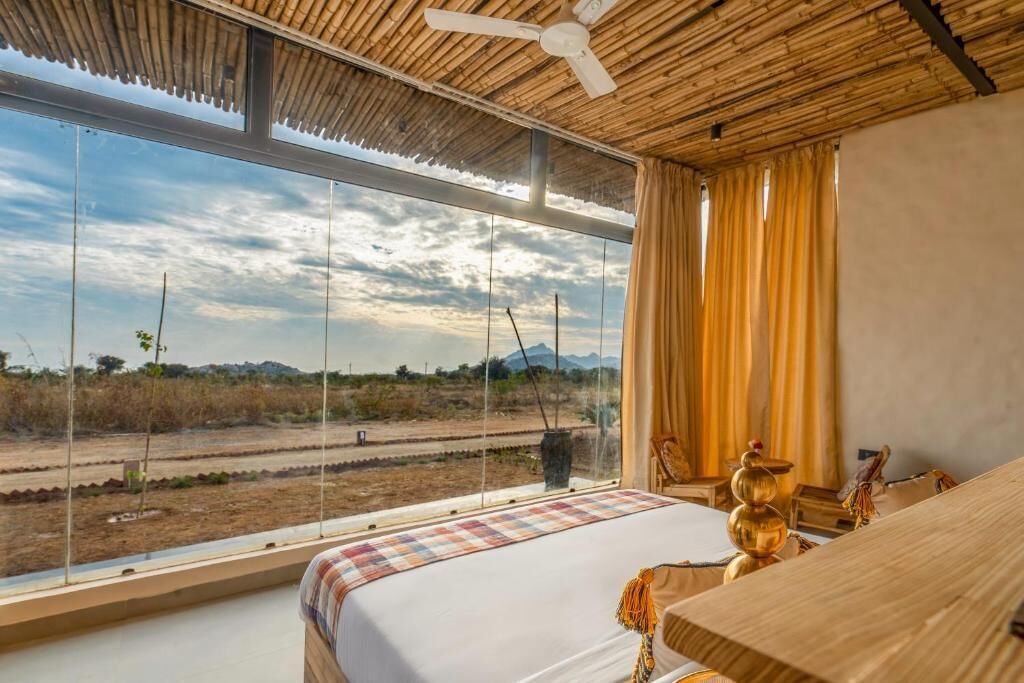 Ein Schlafzimmer mit großem Fenster, einem Bett, Deckenventilator und Blick auf eine Landschaft.