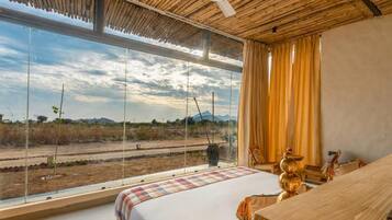 Un dormitorio con un ventanal grande, una cama, un ventilador de techo y vistas a un paisaje.
