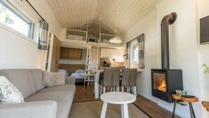 Un intérieur chaleureux avec un canapé, une petite table ronde, un coin cuisine, une chambre en mezzanine et un poêle à bois.