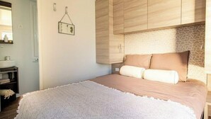 A bedroom with a bed, a wooden wardrobe, a bathroom with a sink, and a wall-mounted picture. - Holiday Home in Olburgen With Terrace (Olburgen)
