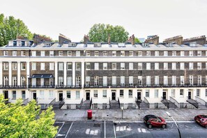A row of terraced houses with uniform architecture, a central staircase, and a parking area in front. - The Guide's Charming Home (London)