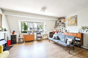 A spacious living room with a sofa, chairs, a coffee table, a bookshelf, and a large window providing a view of the outside. - The Guide's Charming Home (London)