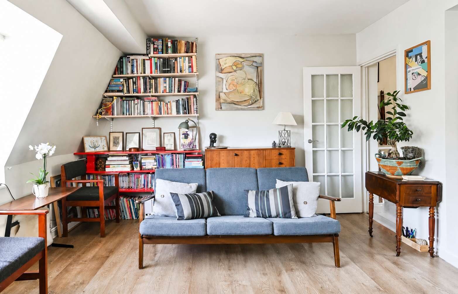 A cozy living room with a blue sofa, wooden bookshelves, a wooden coffee table, and a potted plant.