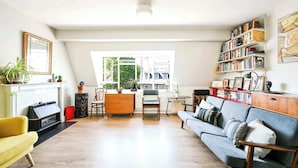 Una sala de estar con chimenea, un sofá, una mesa de comedor con sillas y una estantería.