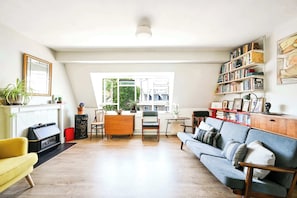 Una sala de estar con chimenea, un sofá, una mesa de comedor con sillas y una estantería.