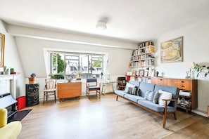 A spacious living room with a sofa, chairs, a coffee table, a bookshelf, and a large window providing a view of the outside. - The Guide's Charming Home (London)