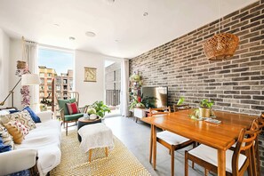 A modern living room with a dining area, a brick wall, and a large window. - Modern Flat with Country Charm (London)