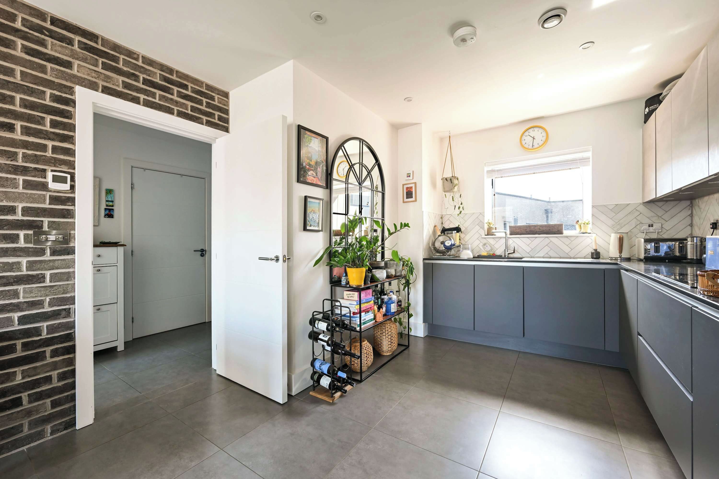 A modern kitchen with grey cabinets, a brick accent wall, a wine rack, and a window with a view.