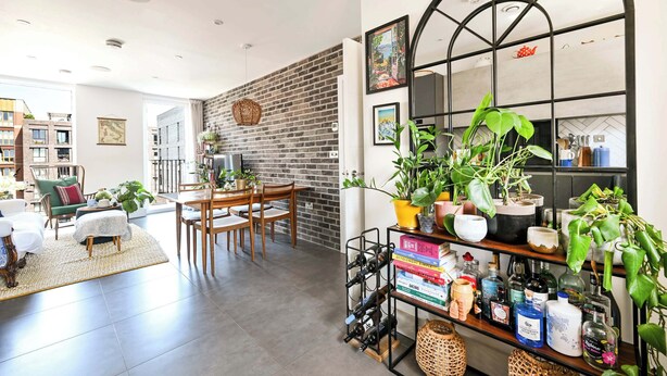 Un salon moderne avec un mur en briques, un coin repas et une bibliothèque contenant des livres et des plantes.