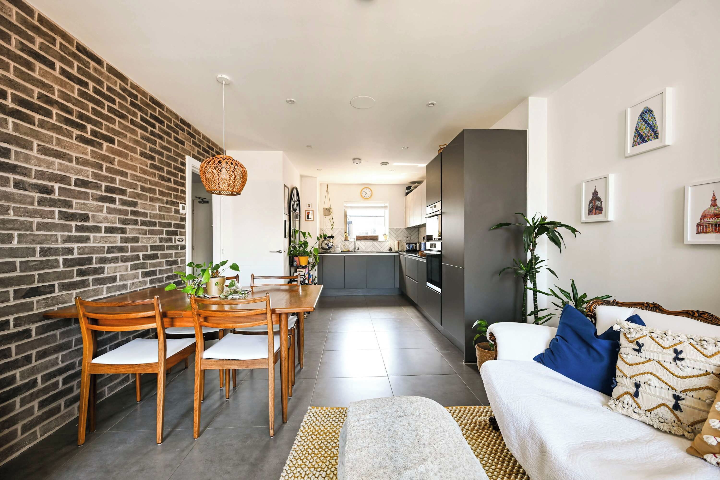 Une cuisine moderne avec des meubles gris, un coin repas avec des chaises et une table en bois, et un salon avec un canapé et des coussins.