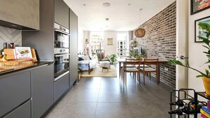 Une cuisine moderne dotée d’appareils électroménagers intégrés, un coin repas avec un mur en briques et un salon comprenant un canapé et une table basse.
