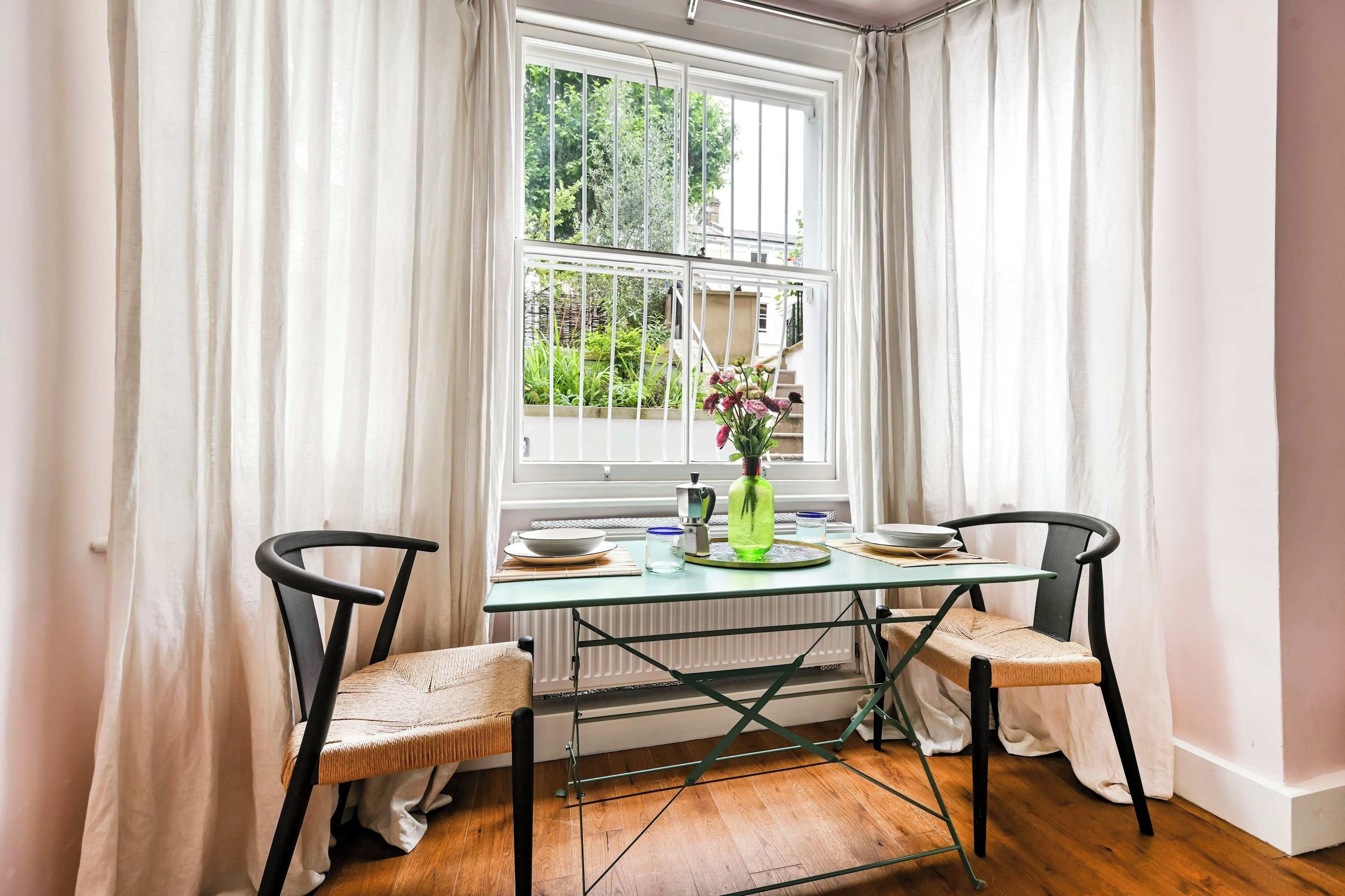 Un coin repas avec une table et des chaises, une fenêtre avec des rideaux et un radiateur.