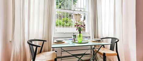 A dining area with a table and chairs, a window with curtains, and a radiator.