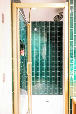 Eine Dusche mit Glastür, grünen Fliesen und einem sichtbaren Duschkopf.