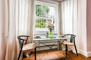 Ein Essbereich mit Tisch und Stühlen, einem Fenster mit Vorhängen und einer Heizung.
