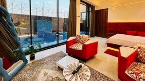 A modern hotel room with a large window, a red sofa, a bed, and a small table. - Luxurious 3-bedroom resort in Haridwar with Private pool, steam and jacuzzi (Haridwar)