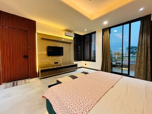 A modern bedroom with a large bed, a TV mounted on the wall, and a view of the outdoors through a large window. - Luxurious 3-bedroom resort in Haridwar with Private pool, steam and jacuzzi (Haridwar)