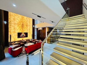A modern living room with a fireplace, red sofas, and a glass staircase.