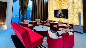 A modern living room with a large TV, red furniture, and a decorative wall. - Luxurious 3-bedroom resort in Haridwar with Private pool, steam and jacuzzi (Haridwar)