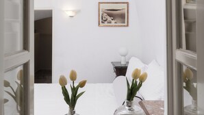 Un couloir menant à une chambre à coucher, où se trouvent un lit, un tableau encadré au mur et deux vases avec des fleurs.