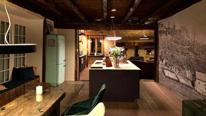 A rustic kitchen with wooden beams, a dining area with a table and chairs, and a refrigerator. - Château de Comborn Riverside Gite with Private River Access in the Vézère Valley (Orgnac-sur-Vézère)