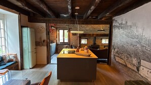 A modern kitchen with a central island, wooden flooring, and a rustic stone wall. - Château de Comborn Riverside Gite with Private River Access in the Vézère Valley (Orgnac-sur-Vézère)