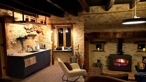 A rustic interior with a kitchen, a cozy seating area, and a wood-burning stove. - Château de Comborn Riverside Gite with Private River Access in the Vézère Valley (Orgnac-sur-Vézère)