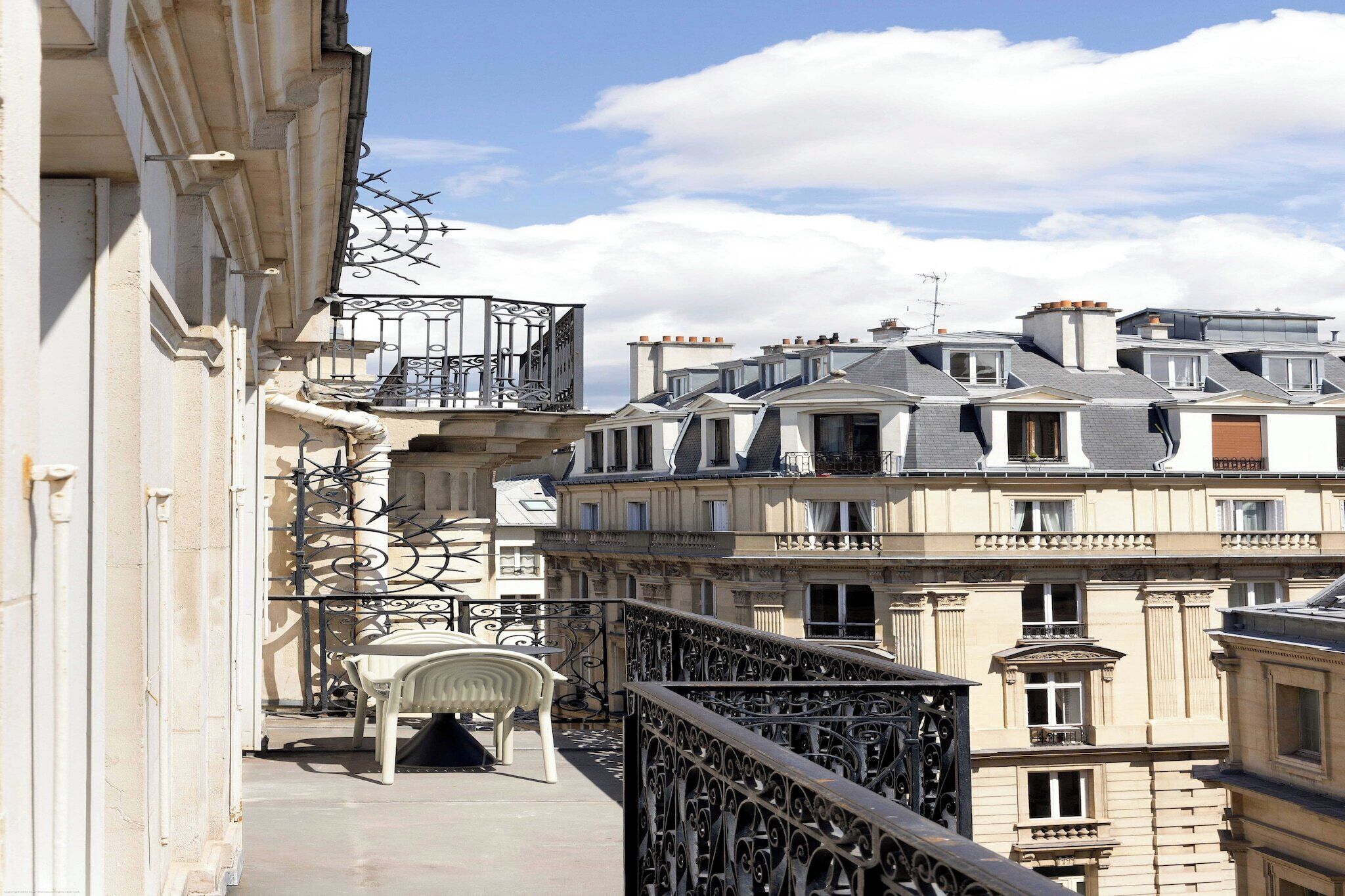 A balcony with a chair, wrought iron railing, and a view of adjacent buildings.