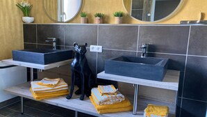 Ein modernes Badezimmer mit zwei Waschbecken, einer Statue eines schwarzen Hundes und Handtüchern auf einem Regal.