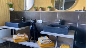 A modern bathroom with two sinks, a black dog statue, and towels on a shelf.
