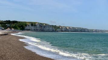A coastal beach with white cliffs, a pebbly shore, and a clear sky.