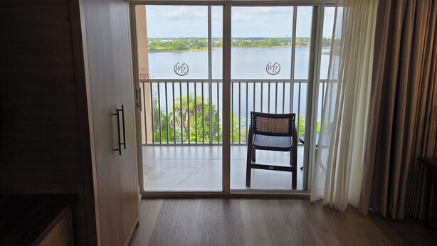 Una habitación con puerta corrediza de vidrio que da a un balcón con vista a una masa de agua.