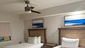 Una habitación de hotel con dos camas de madera, un ventilador de techo, una mesita de noche y un cuadro en la pared.