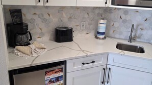 Una cocina con gabinetes blancos, un refrigerador de acero inoxidable, una cafetera, un tostador, un microondas y un lavaplatos.