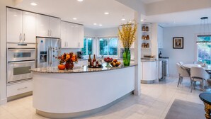 A modern kitchen with a curved island, built-in appliances, and a dining area with a view. - Contemporary Bellevue Home with Panoramic Lake & Mountain Views (Bellevue)