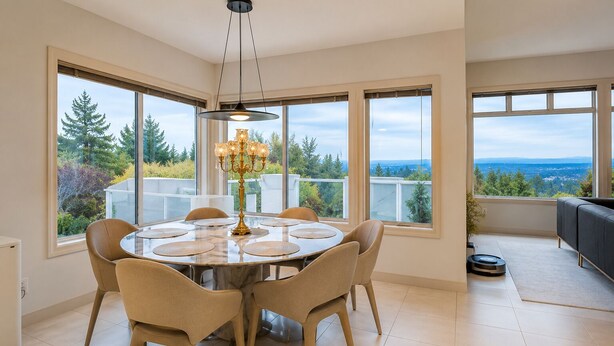 A dining area with a round table, six chairs, a chandelier, and large windows offering a view of trees and a distant landscape. - Contemporary Bellevue Home with Panoramic Lake & Mountain Views (Bellevue)