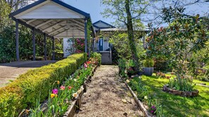 A garden pathway leading to a covered structure with a wooden bench and a variety of flowers and plants. - Wisteria Cottage in Leura (Leura)