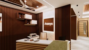 Un espace d’accueil doté d’un comptoir en bois, d’une plaque nominative fixée au mur portant l’inscription « Aranya », et d’un design moderne au niveau du plafond.