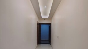 Un couloir avec un luminaire au plafond, une porte au fond et un interrupteur sur le mur.