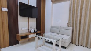Un salon moderne avec une table basse en verre, un canapé, un téléviseur fixé au mur et un meuble en bois.