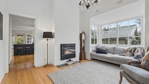 A living room with a fireplace, a sofa, a clock, and a chandelier. - Brixton Cottage in Katoomba (Katoomba)